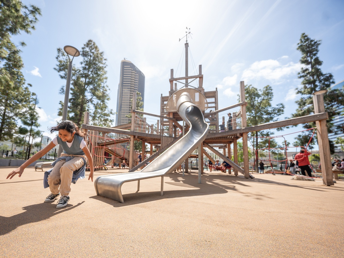 Laughing girl in front of tunnel slide and play pyramid with vertical climbing net in the background © Daniel Perales