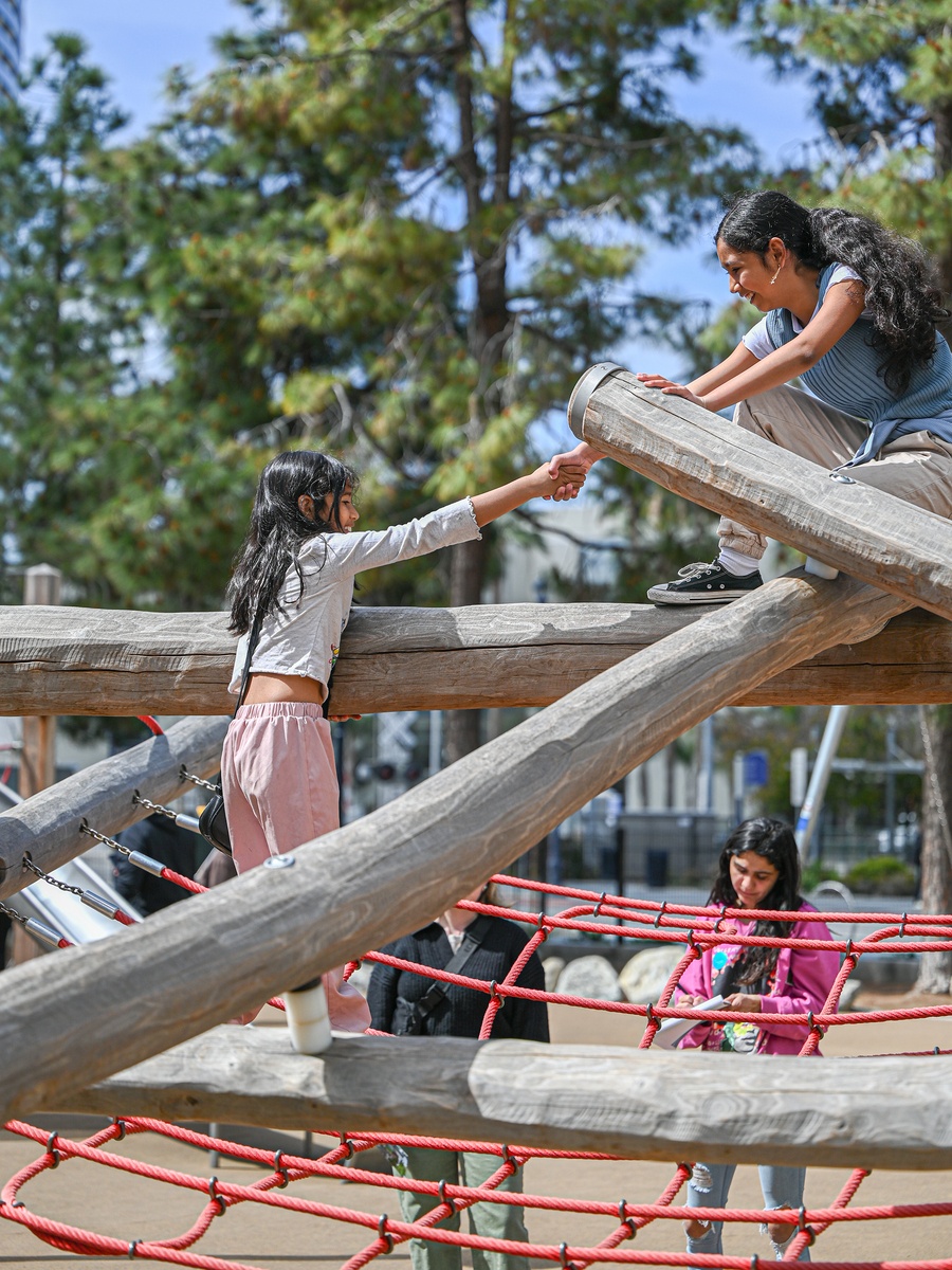 Girl and young woman shake hands on climbing structure © Daniel Perales