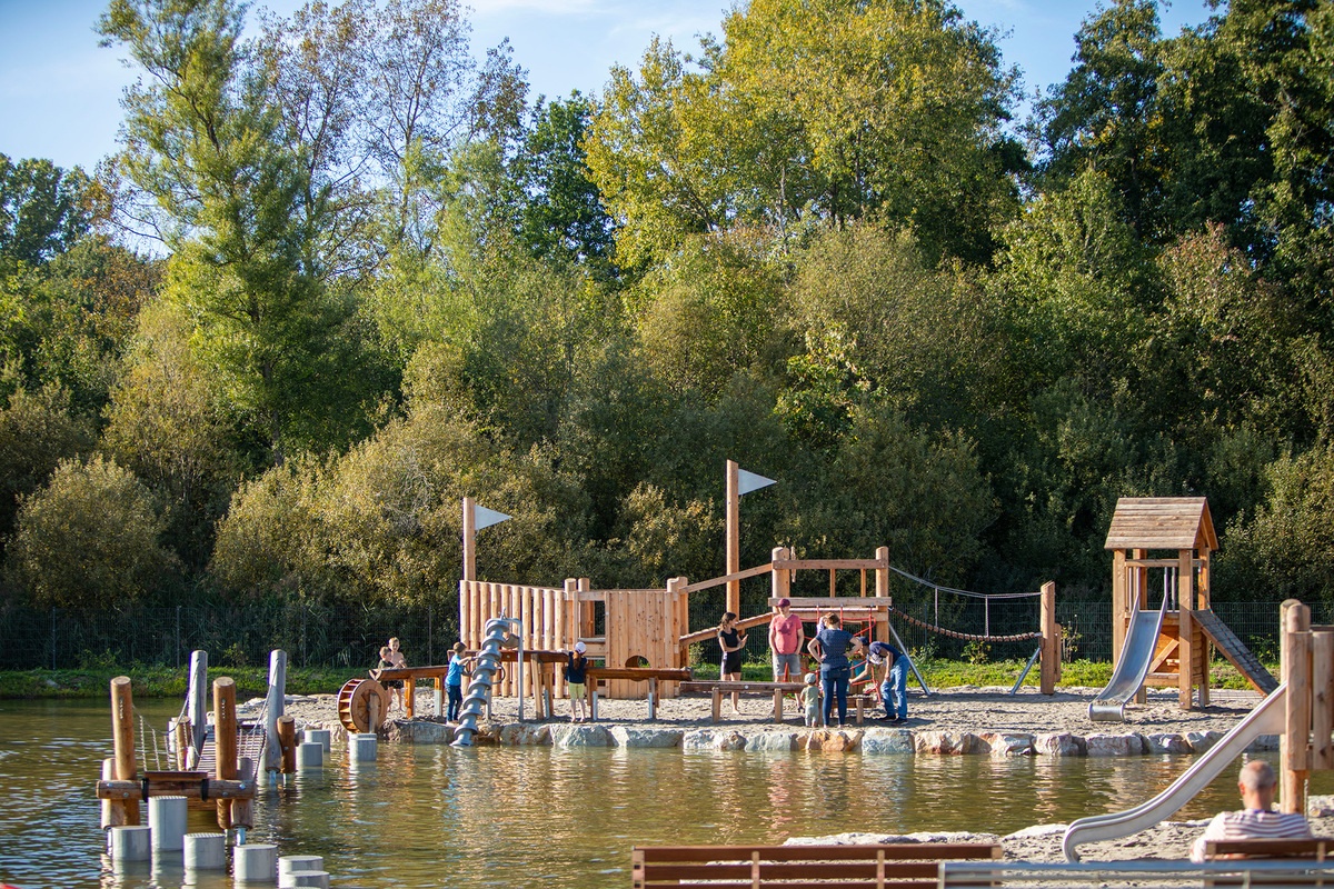 Kinder spielen auf einem Spielplatz mit Spielgeräte aus Holz sowie mit Wasserspielelementen am Bostalsee.