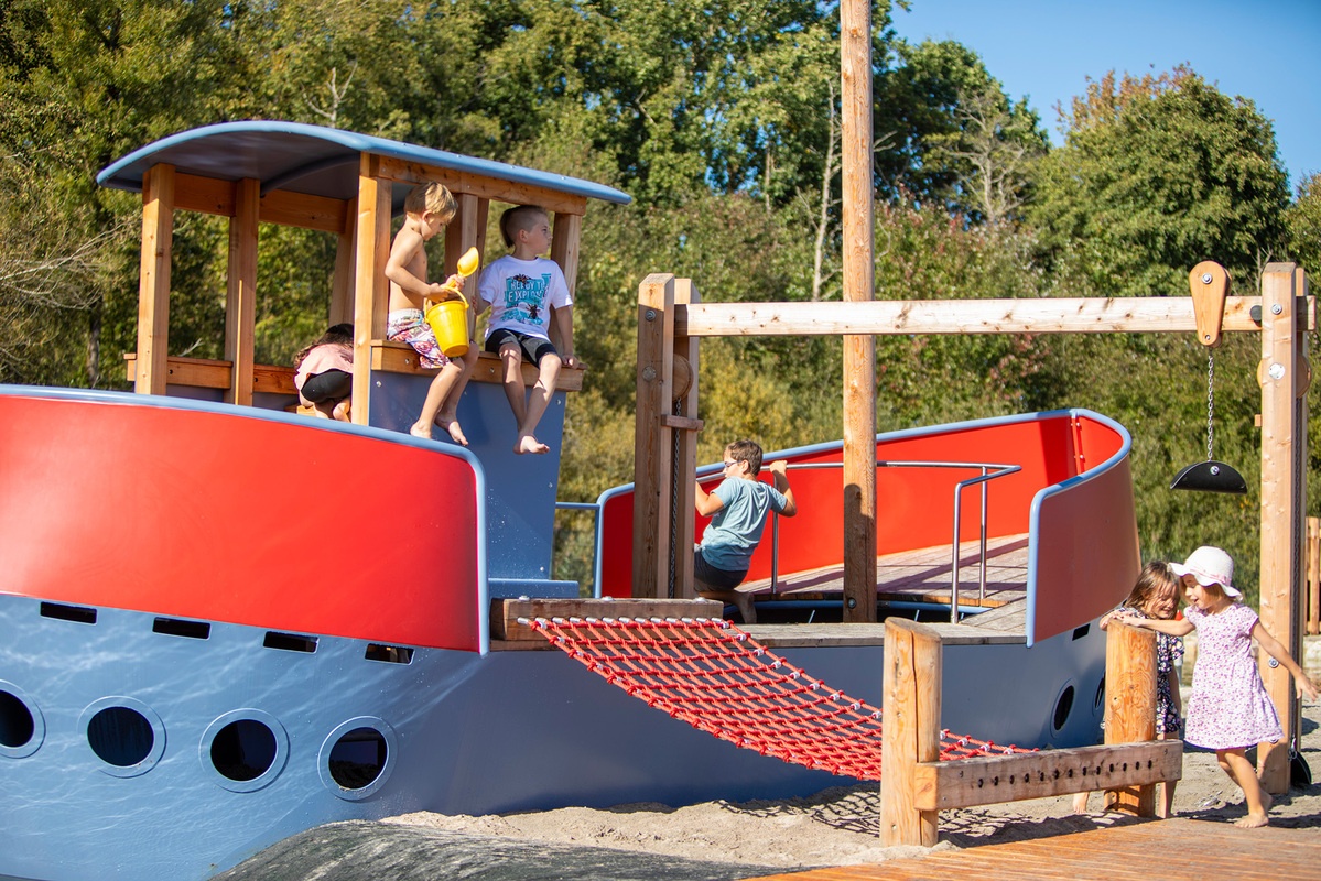 Kinder spielen auf einem blau-roten Metallschiff mit rotem Kletternetz.