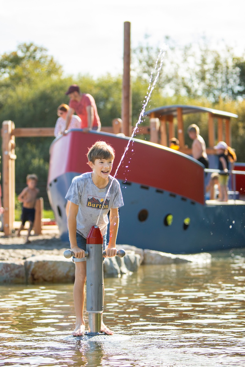 Kind spielt mit Spritzpumpe mit rotem Kopf am Bostalsee. 