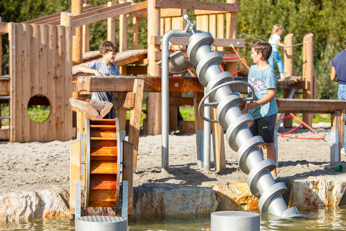 Kinder spielen mit verschiedenen Wasserspielgeräte, darunter Archimedischer Schraube und Mühlenrad am Bostalsee.