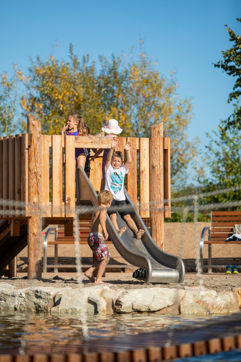 Kind rutscht auf einer Metallrutsche von einer Spielplattform aus Holz am Bostalsee.