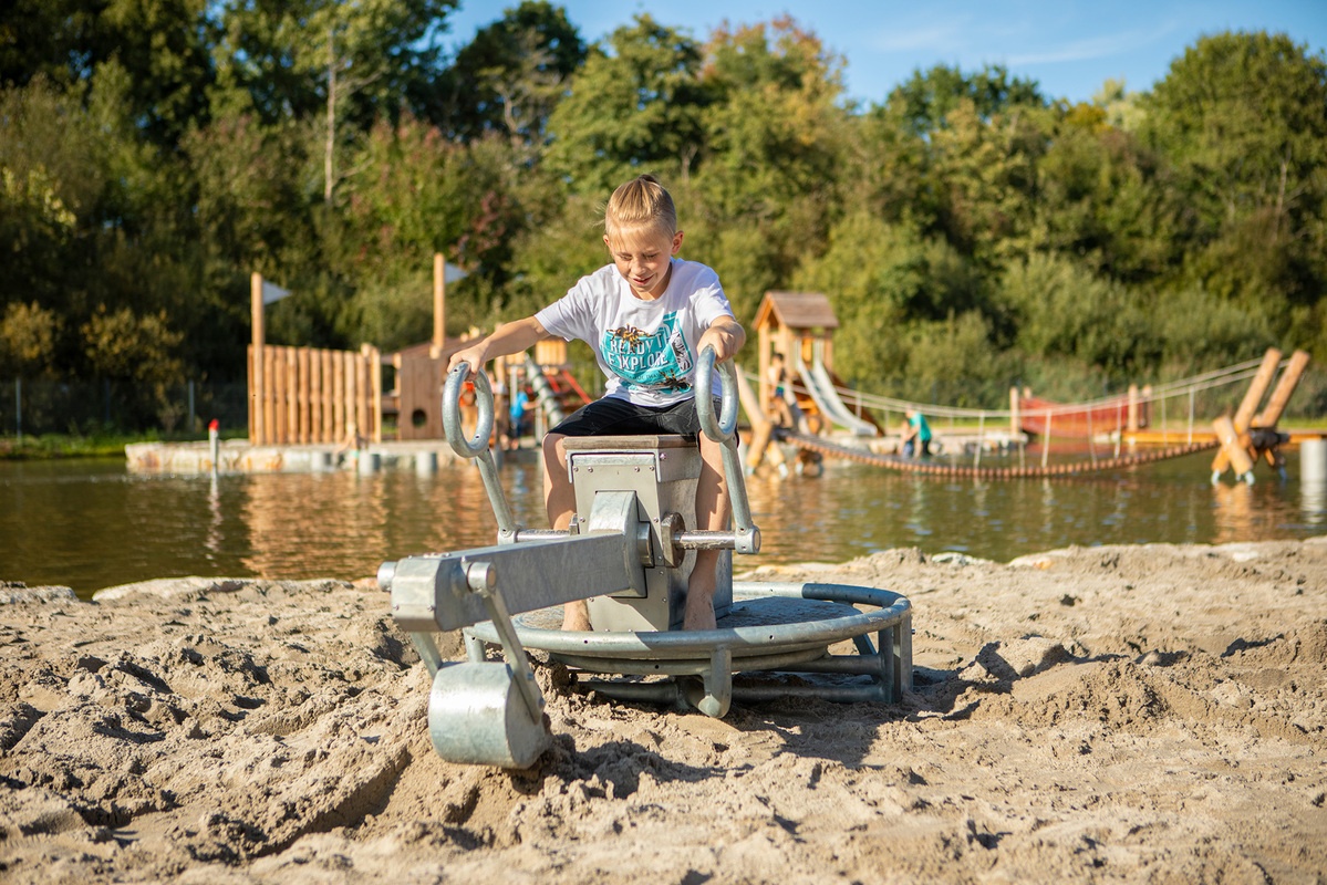 Kind spielt mit einem Bagger mit Sand auf dem Spielplatz am Bostalsee. 