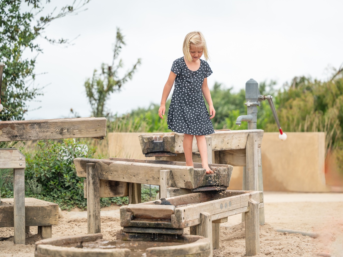Child balancing on a wooden water channel at an adventure playground. The Golden Gate Bridge in the background.