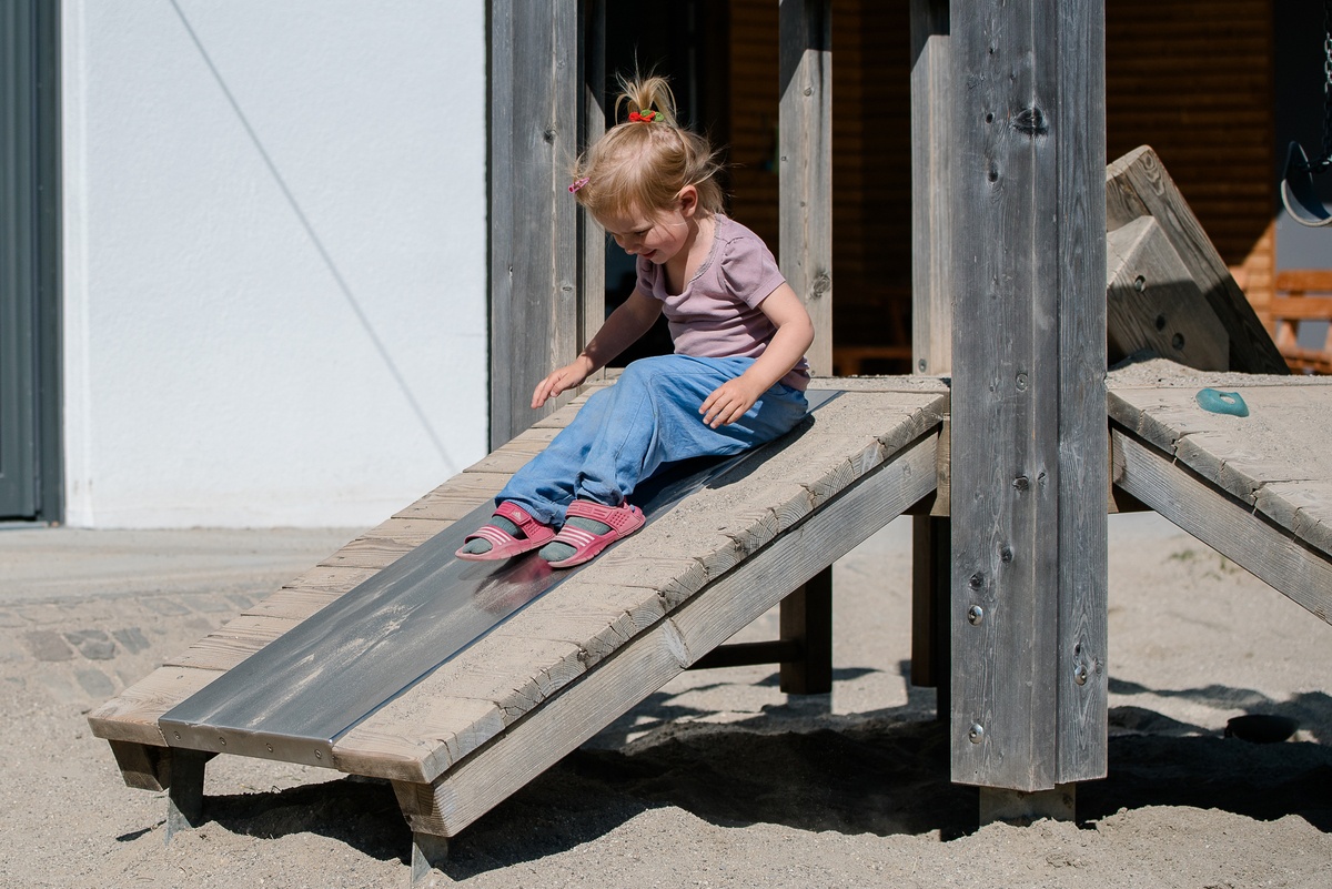 Kind rutscht über eine niedrige glatte Oberfläche von der Kleinkind-Plattformhütte.