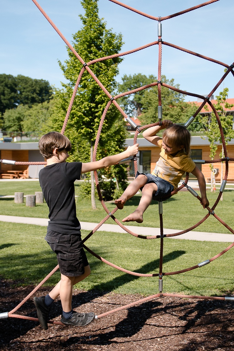 Kinder klettern in einem großen roten Spinnennetz aus Seil.