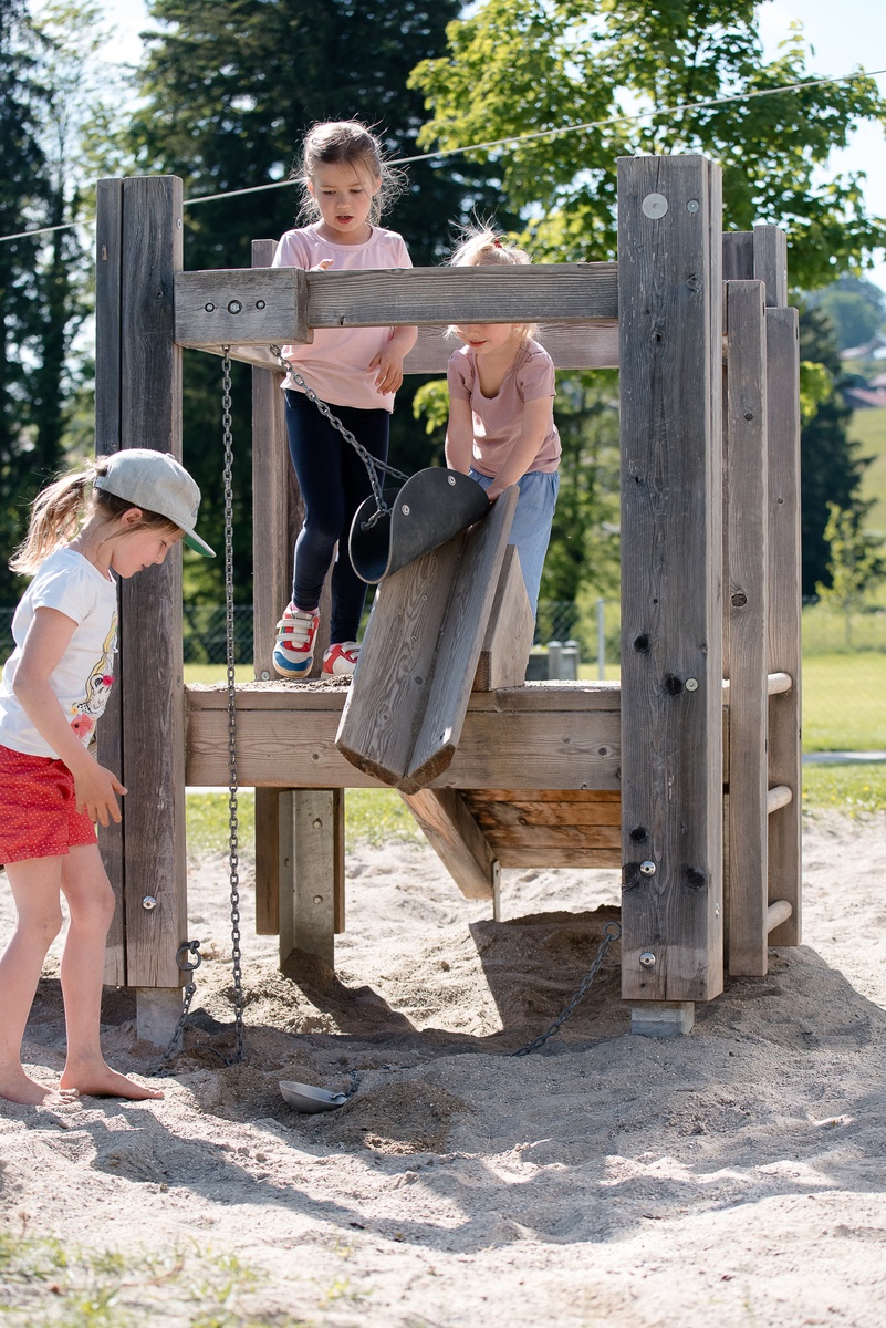 Several children are playing on and around a platform hut with a sand hoist with shovel.