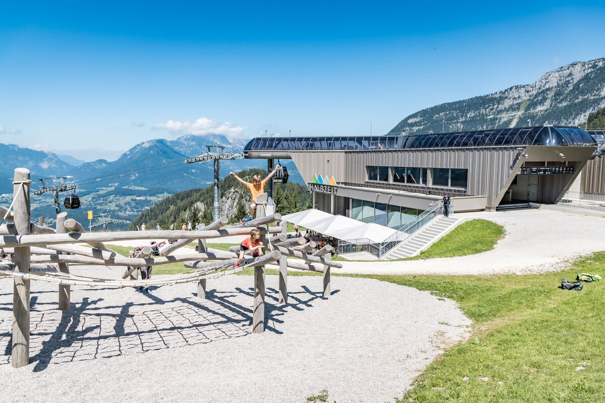 Children balance and climb on a climbing structure made of round robinia wood. The Berchtesgaden Alps in the background.