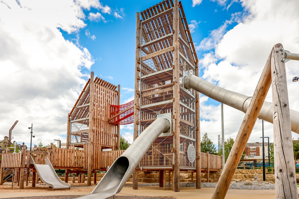Two towers connected by a red suspension bridge with tunnel slides.  