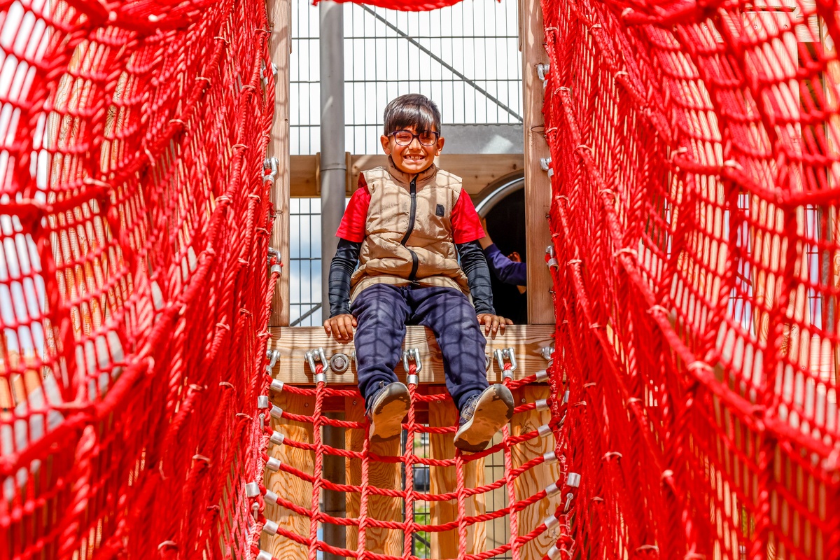 Child climbing through the mesh red net suspension bridge.