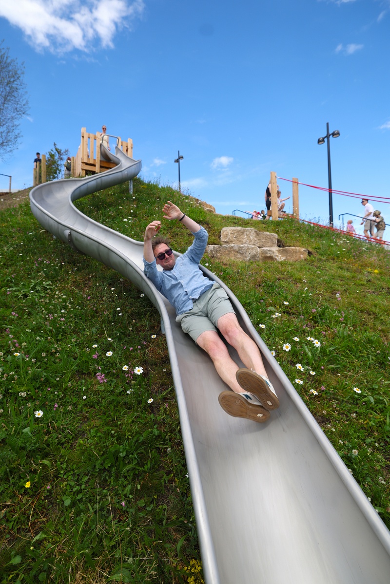 Man slides down metal, curved slide.