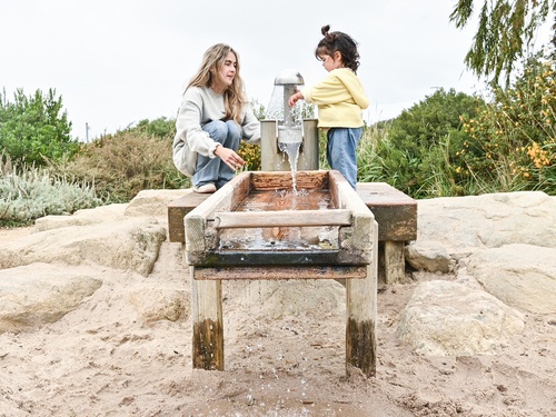 Kinder spielen gemeinsam an einer Spielplatz-Wasserpumpe mit Auffangbecken, moderner Wasserspielplatz mit Blick auf die Golden Gate Bridge.