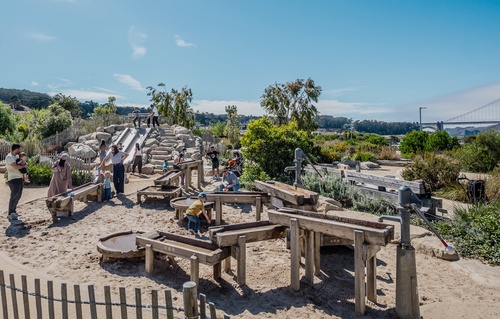 Großer Wasserspielplatz mit mehreren Richter Wasserspielgeräten, spielende Kinder und die Golden Gate Bridge im Hintergrund.