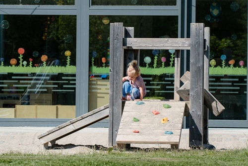 Child sliding down a low, smooth surface from a toddler’s platform hut.