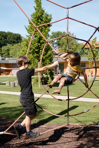 Children climb in a large red spider's web made of rope.