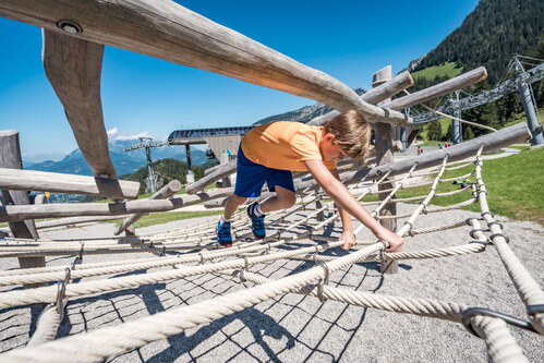 Kinder balancieren und klettern auf einer Kletterstruktur aus Robinienrundhölzern. Die Berchtesgadener Alpen im Hintergrund.