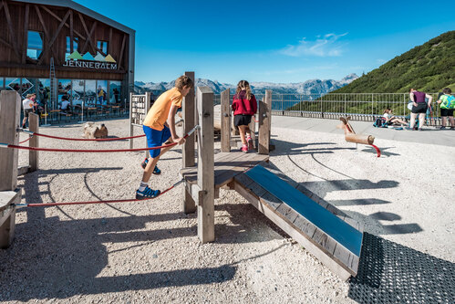 Kinder laufen über den Kleinkindparcours Variante 01 mit Laufseil und Handseilen. Im Hintergrund ein Schwingpferd und Bergpanorama.