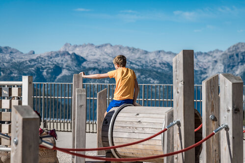 Child sitting on a crawling barrel of the  Richter Totter Trail Variant 01  with a view of the mountain panorama in the background. 