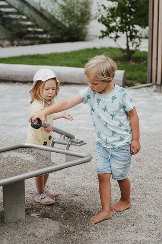 Zwei Kinder spielen an einem mit Sand befüllten Wasserbecken mit Stauklappe.