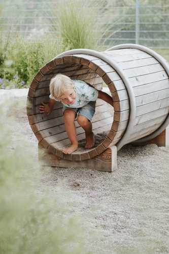 Kind klettert durch das Krabbelfass aus Holz.