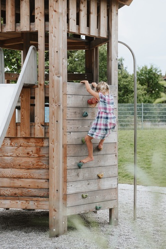 Child climbing on a climbing wall of the large hexagonal hut with roof.
