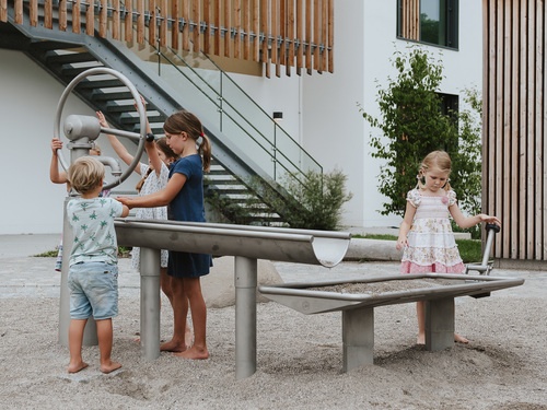 Children playing at a water flooter with crank handle pump and water basin with seal.
