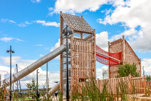 Two towers connected by a red suspension bridge with one tunnel slide attatched.  