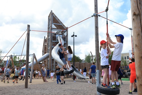 Children run across stockholm play space while four children stand laughing on the tire swings.