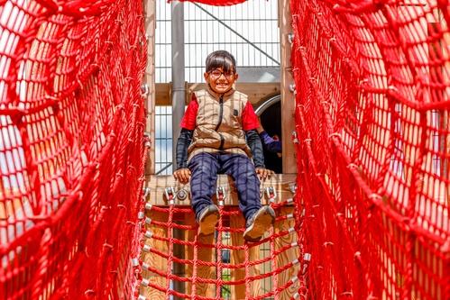 Child climbing through the mesh red net suspension bridge.
